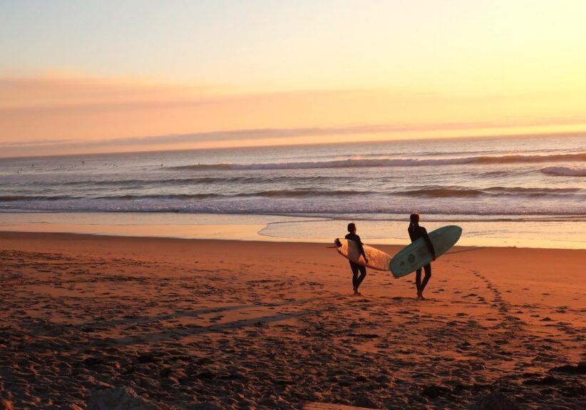 two surfers walking on sand going on water